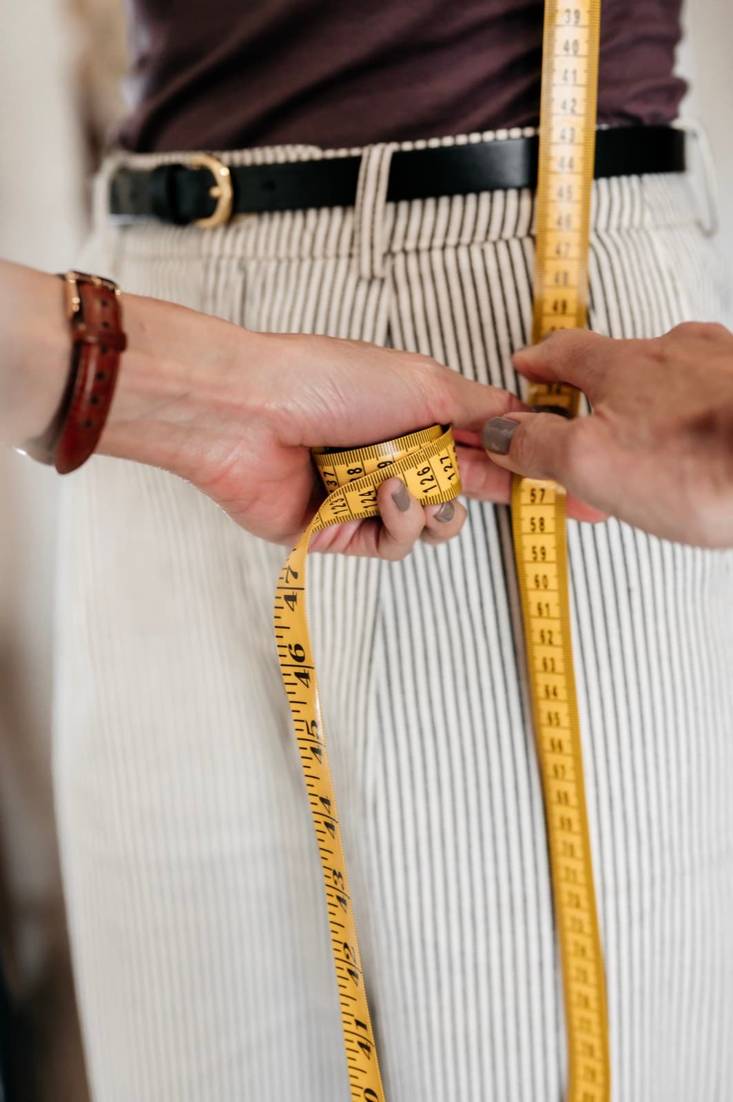 A tape measure held at the waist of cream trousers